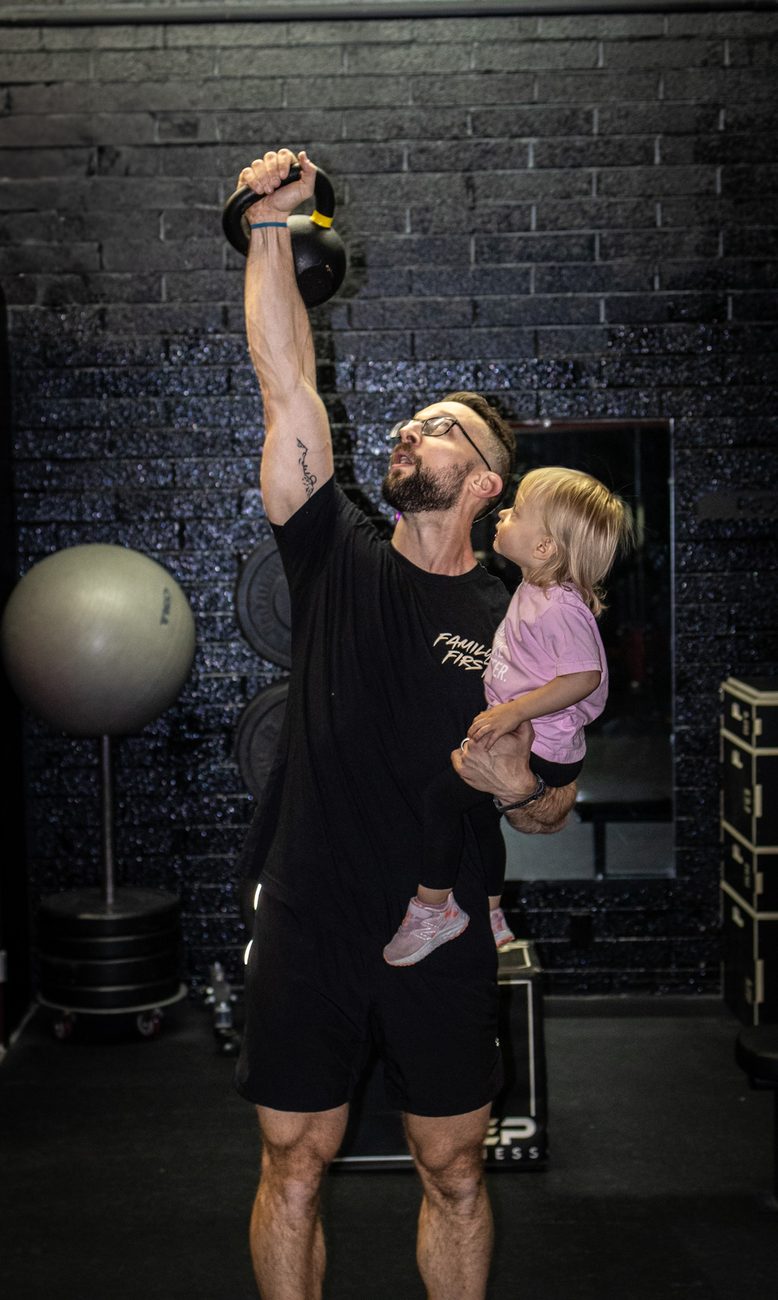 David pressing overhead while holding his daughter